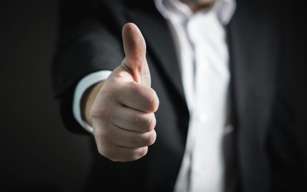 Accrédité A close-up of a man's thumbs up gesture, symbolizing success and agreement.